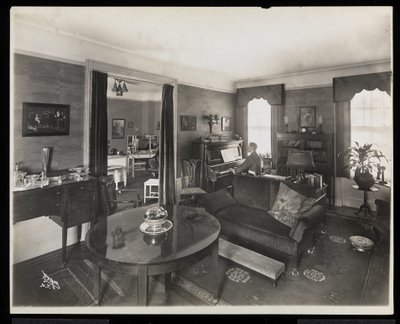 Een man die piano speelt in een woonkamer van de A.C. Cronin-residentie, 1915-16 door Byron Company